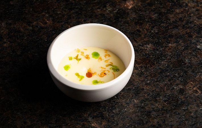 Helle Cremesuppe mit Kräuteröl-Tropfen in weißer Schale