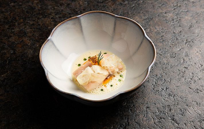 Fischstücke in heller Schaumsauce mit Kräutern in weißer Schale, Nahaufnahme