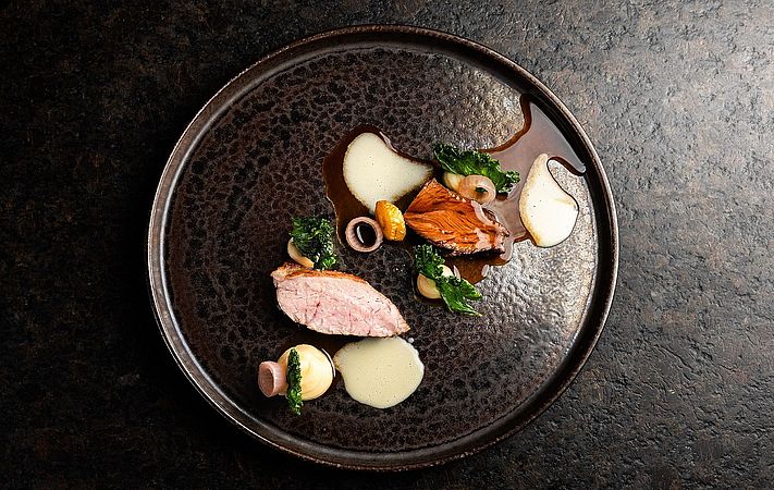 Geflügelbrust mit Cremes, Kräutern und Sauce auf dunklem Teller, von oben