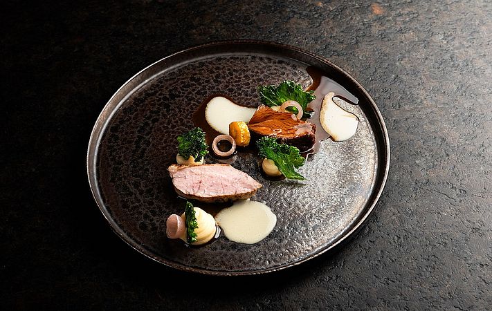 Geflügelbrust mit Cremes, Kräutern und Sauce auf dunklem Teller